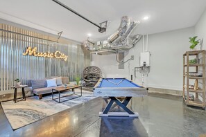 Ein modernes Wohnzimmer mit Billardtisch, einer Couch, einem Sessel und einer Neonleuchtreklame.