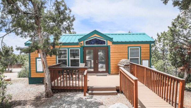Une cabane en bois avec un toit vert, une porte d’entrée et une terrasse en bois.