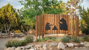 Une clôture en bois ornée de silhouettes d’ours, entourée de rochers et de plantes.