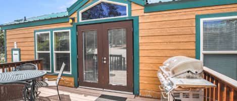 Une cabane en bois dotée d’une terrasse, d’un barbecue et d’une porte avec des panneaux de verre.