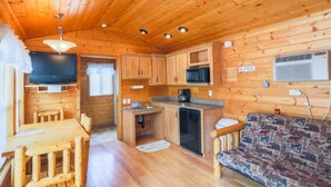 L’intérieur d’un chalet en bois comprend une table à manger, un canapé, un coin cuisine et des ventilateurs de plafond.