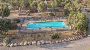 Une piscine entourée de chaises longues et d’une terrasse en bois, avec des arbres et une clôture en arrière-plan.