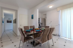 Un coin repas avec une table dressée pour quatre personnes, des chaises, un réfrigérateur et une fenêtre avec des rideaux.
