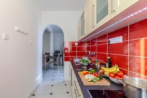 A modern kitchen with red tiles, a cutting board with vegetables, and a pot on the stove. - Káli Retreat Apartments (Zanka)