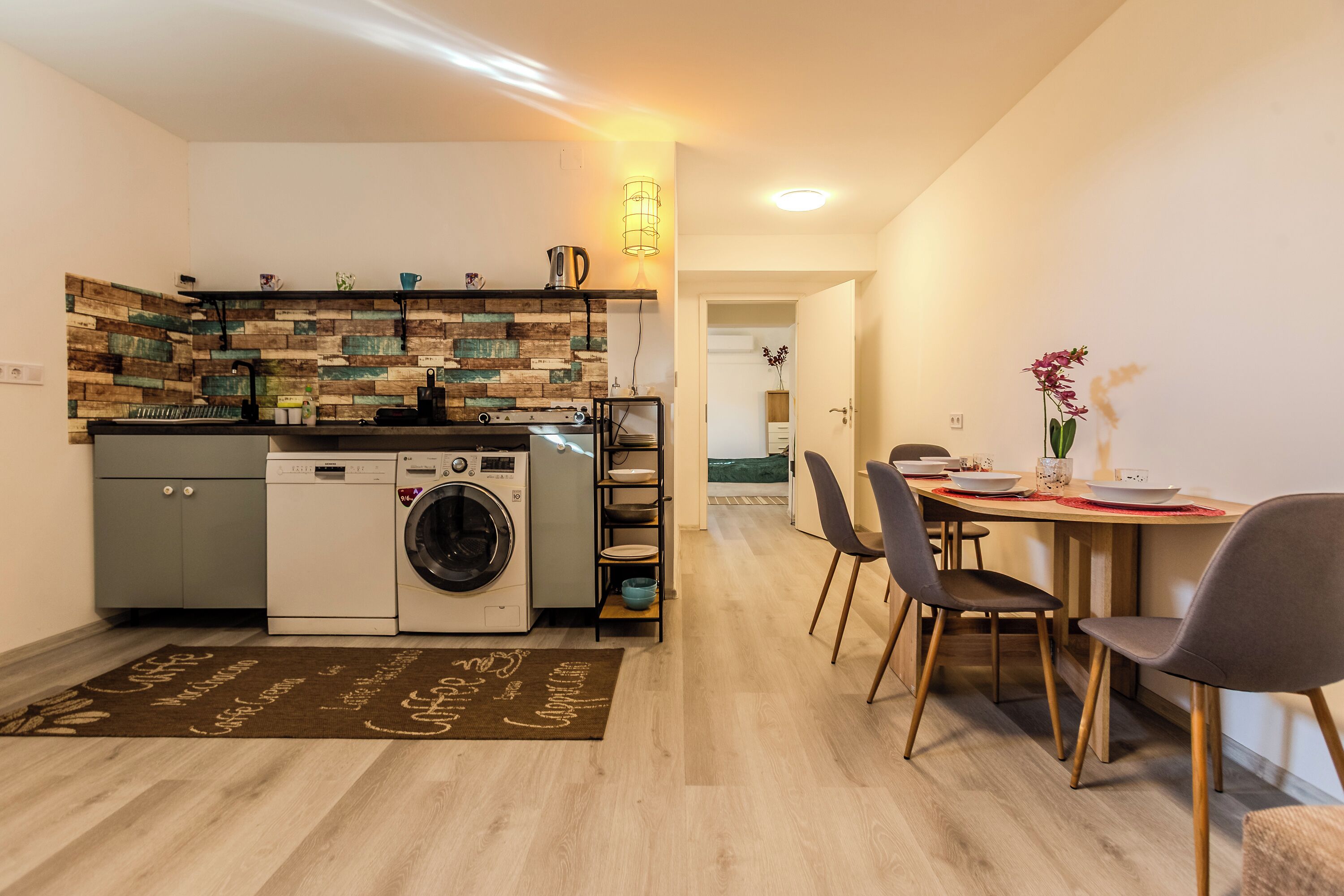 A compact kitchen with a washing machine, a coffee machine, and a built-in oven.