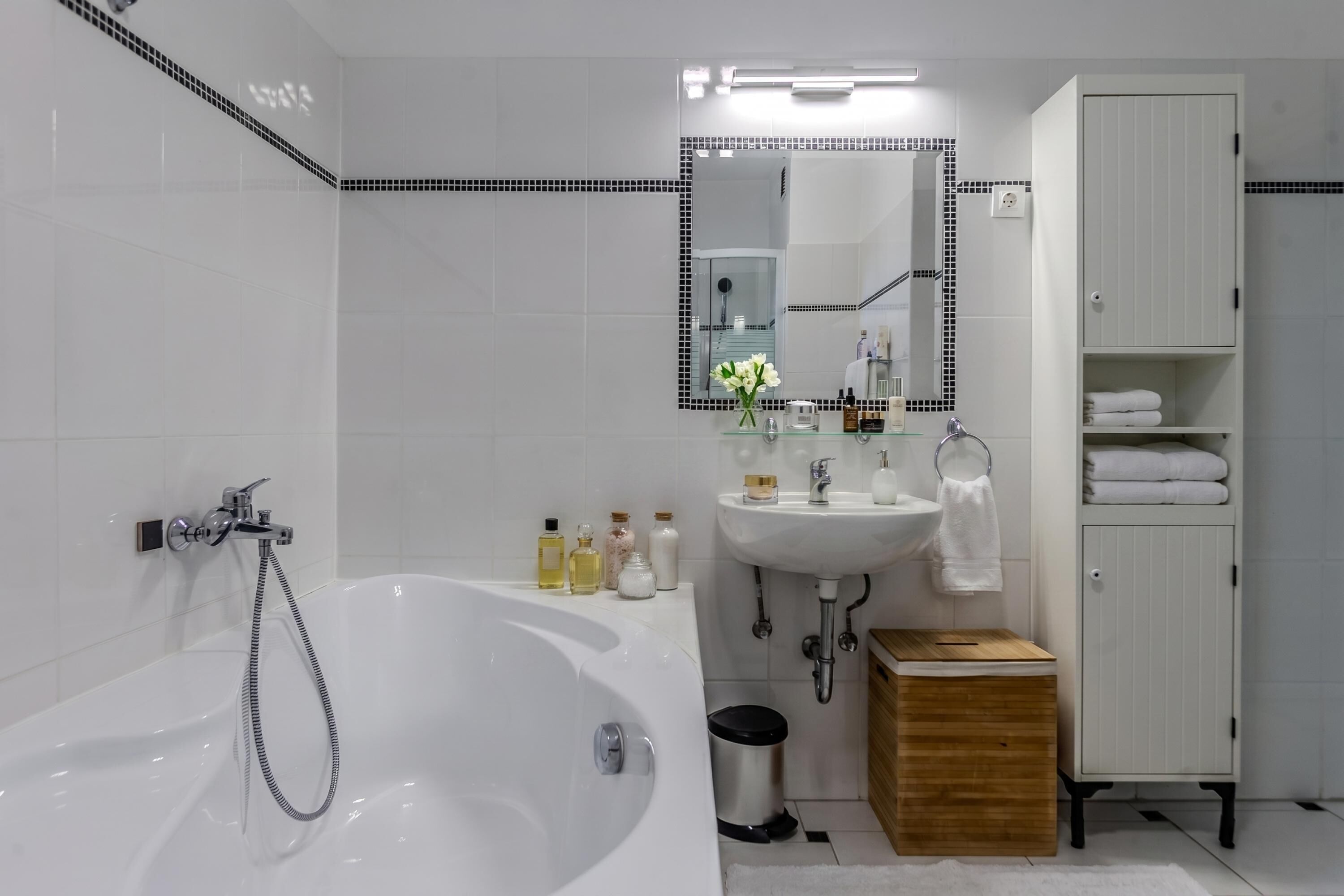 A modern bathroom with a bathtub, sink, mirror, and storage cabinet.