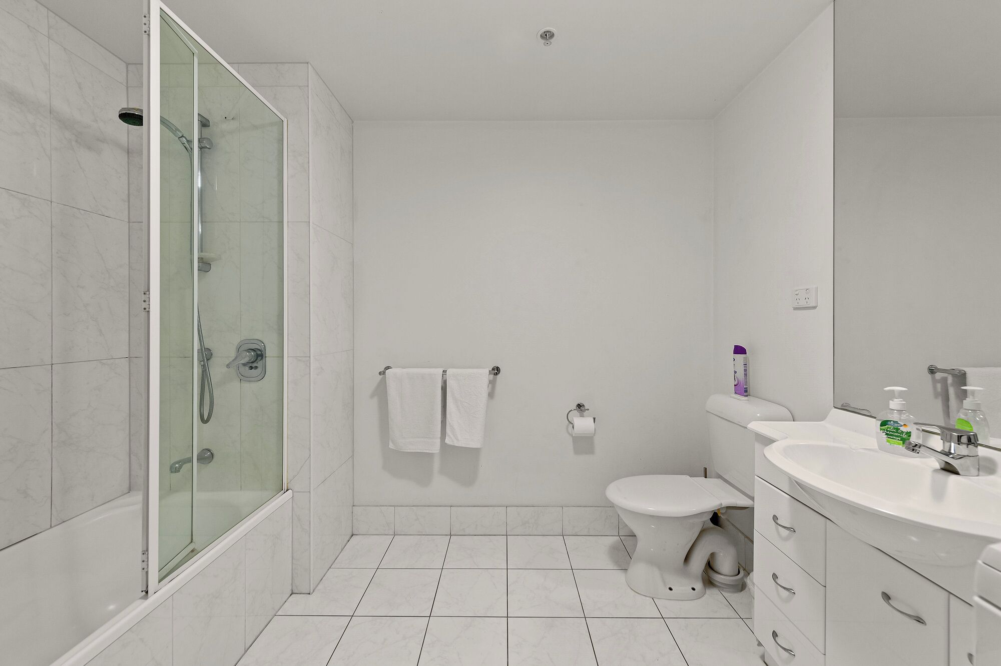 A modern bathroom with a glass-enclosed shower, a toilet, and a sink with a mirror.