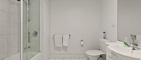 A modern bathroom with a glass-enclosed shower, a toilet, and a sink with a mirror.