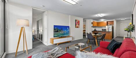 Una sala de estar moderna con un sofá rojo, un televisor y un comedor con cocina al fondo.