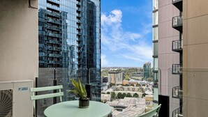 Un balcon avec une table et des chaises, un pot de fleurs et une vue sur les bâtiments environnants.
