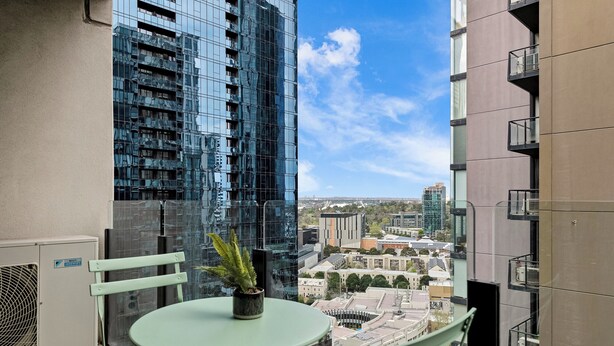 A balcony with a table and chairs, a potted plant, and a view of surrounding buildings. - Exclusive Stays - The Summit (Southbank)