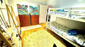 A room with bunk beds, a ladder, a colorful painting, and a woven rug.