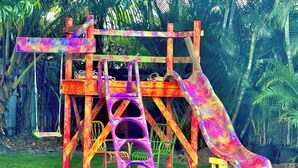 A colorful playground structure with slides and swings, surrounded by lush greenery.
