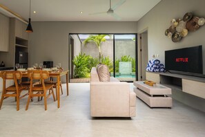 Una sala de estar moderna con un sofá, una mesa de comedor, sillas, un televisor de pantalla plana y un ventilador de techo.