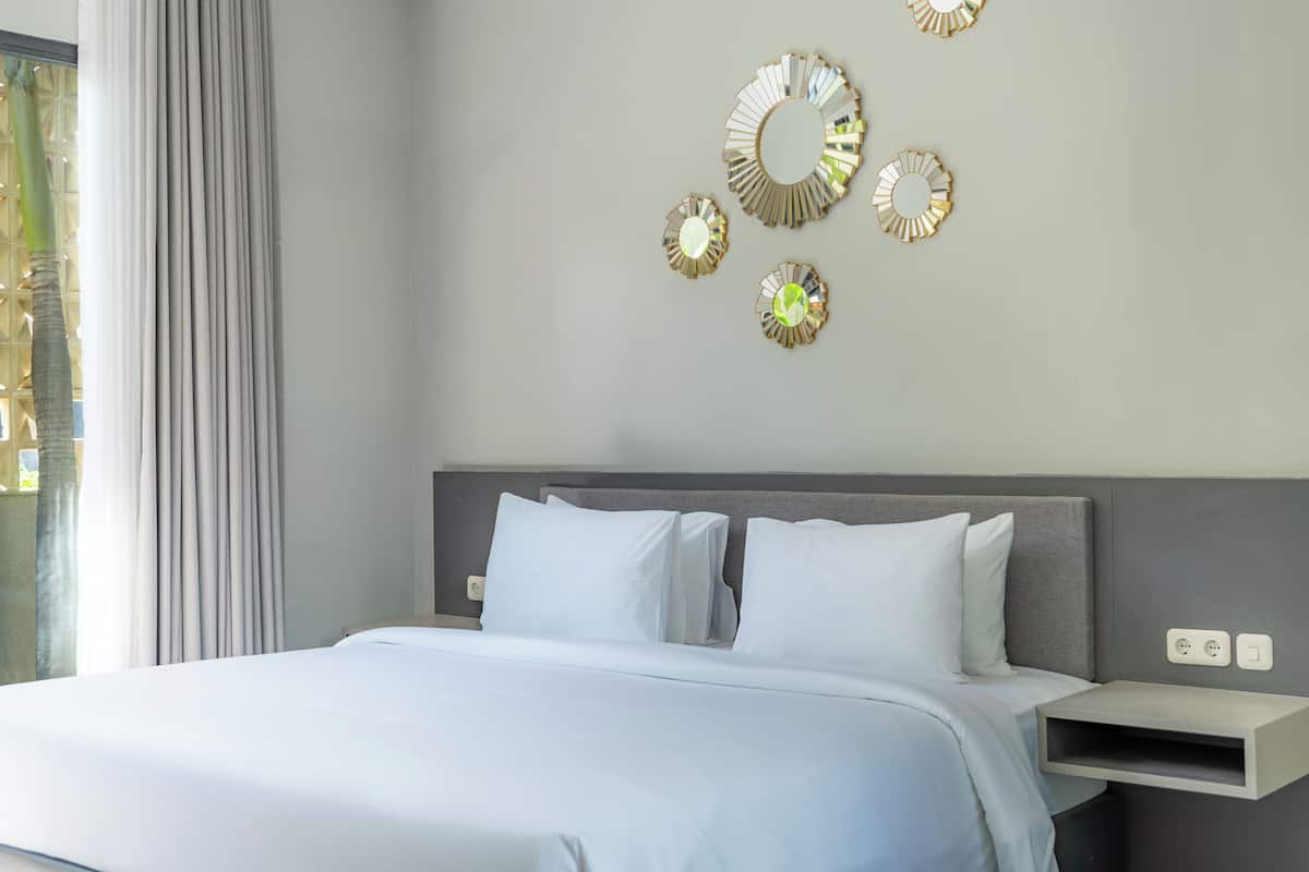 Une chambre d’hôtel moderne, équipée d’un lit, d’une table de chevet et de miroirs décoratifs sur les murs.