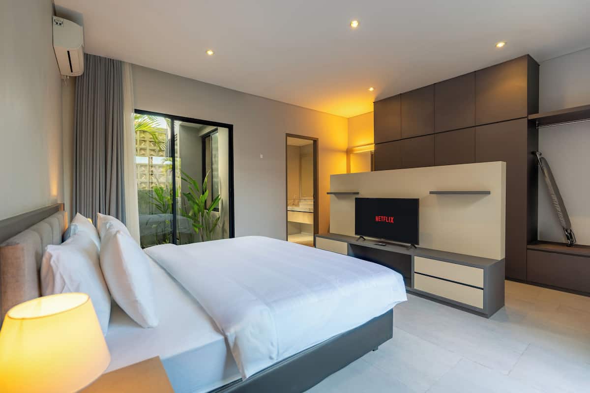 Une chambre d’hôtel moderne équipée d’un lit, d’une télévision, d’un bureau et d’une porte coulissante donnant sur l’extérieur.