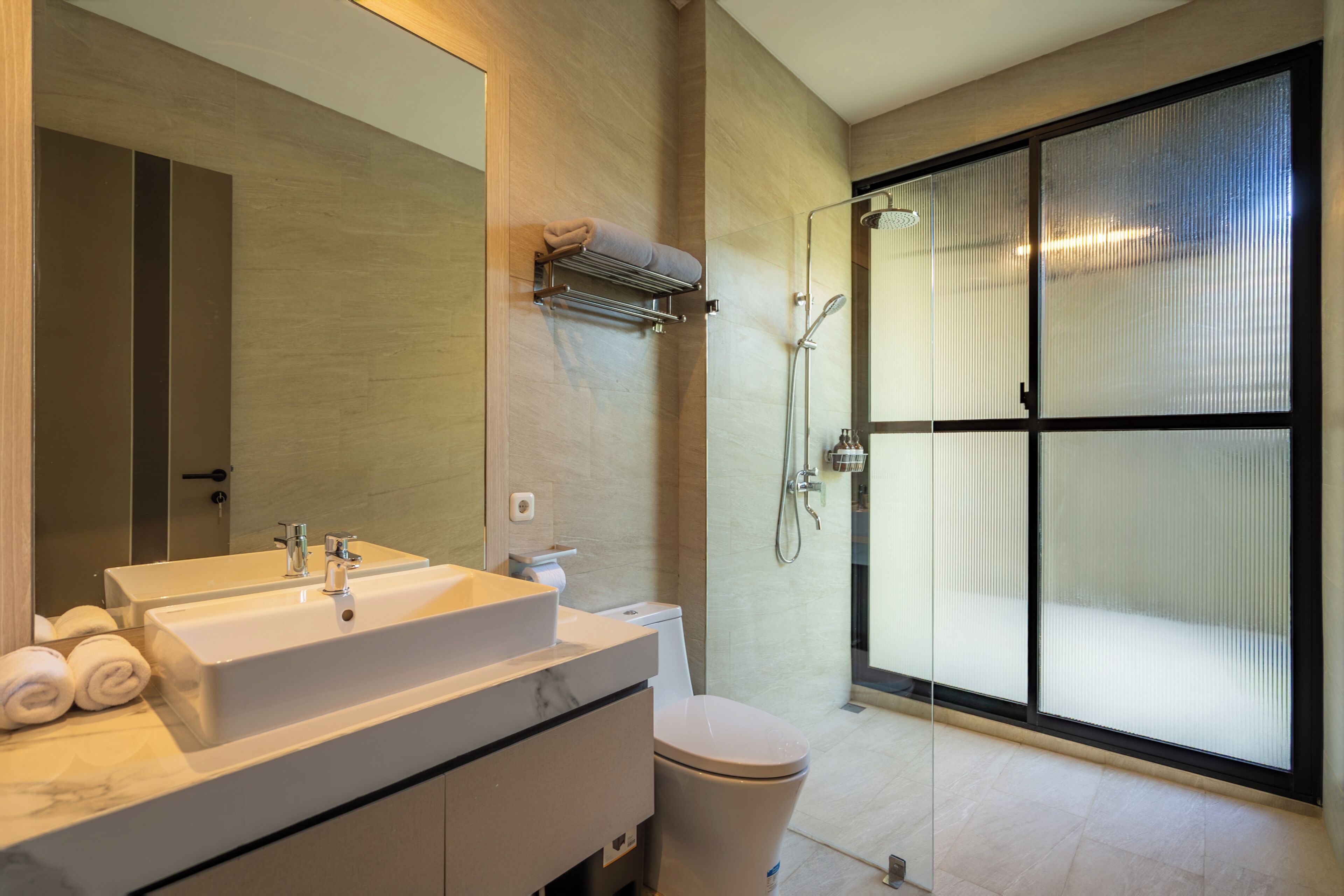 A modern bathroom with a large mirror, dual sinks, a toilet, and a glass-enclosed shower area.