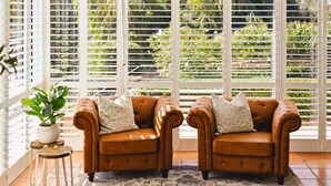 Two brown leather armchairs with patterned cushions, a potted plant, and a patterned rug in a room with large windows and a white railing.