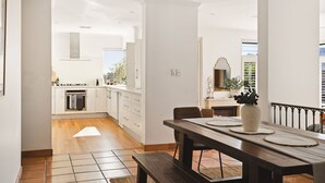A modern kitchen with white cabinets, a dining area with a wooden table, and a view of the outdoors.