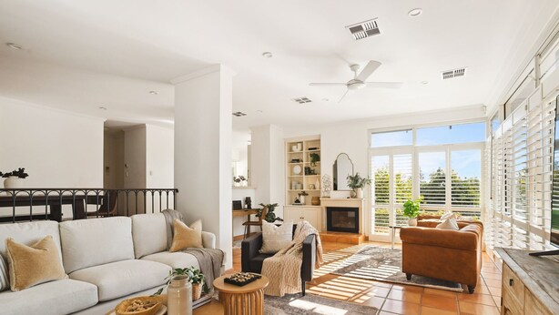 A spacious living room with a fireplace, a sofa, a coffee table, and a dining area with a railing.