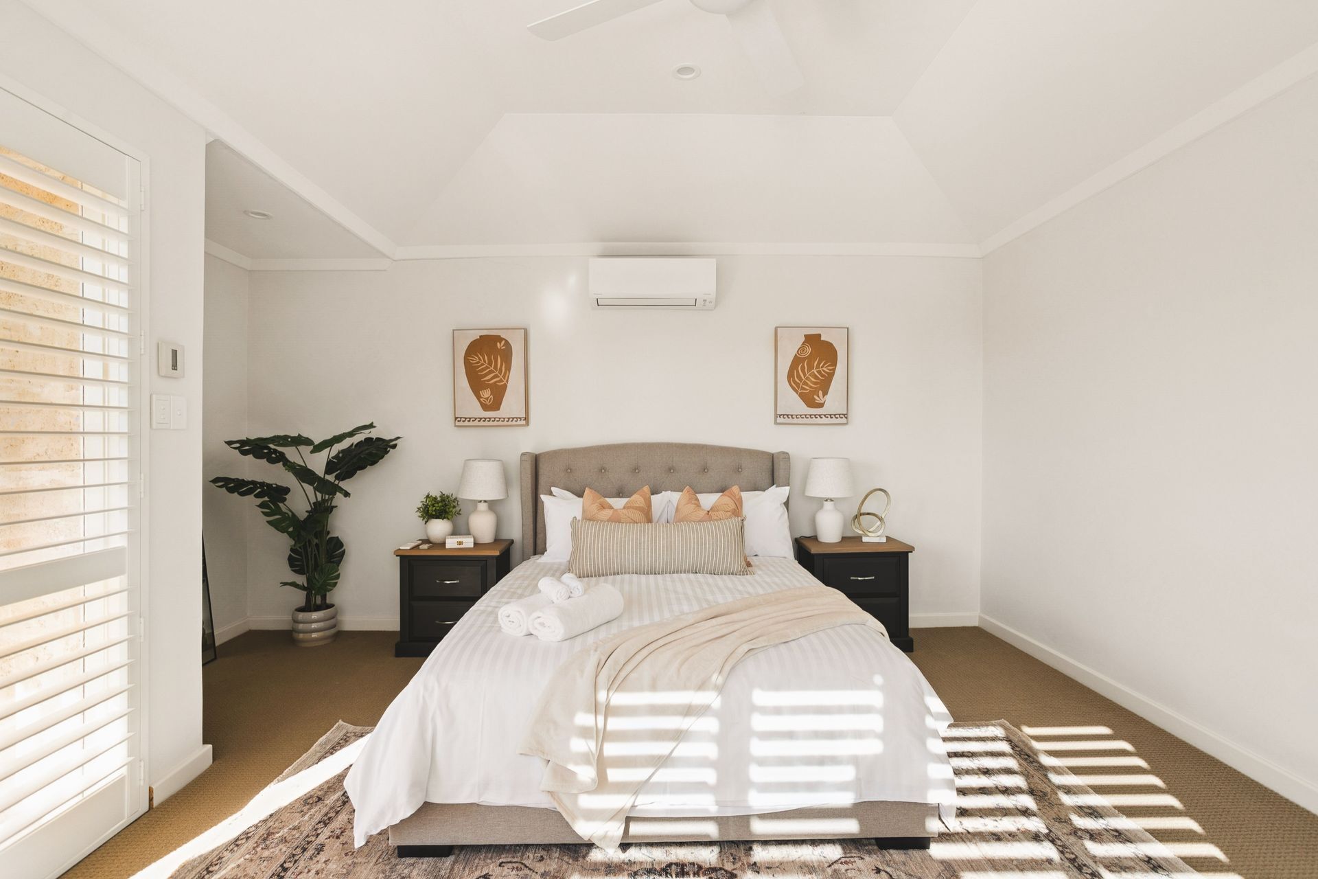 Une chambre à coucher comprenant un lit, des tables de chevet, une plante et deux unités de climatisation fixées au mur.