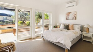 A bedroom with a bed, nightstands, a ceiling fan, and a view through large windows.