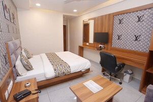 Una habitación de hotel con cama, escritorio, silla, televisor y espejo.