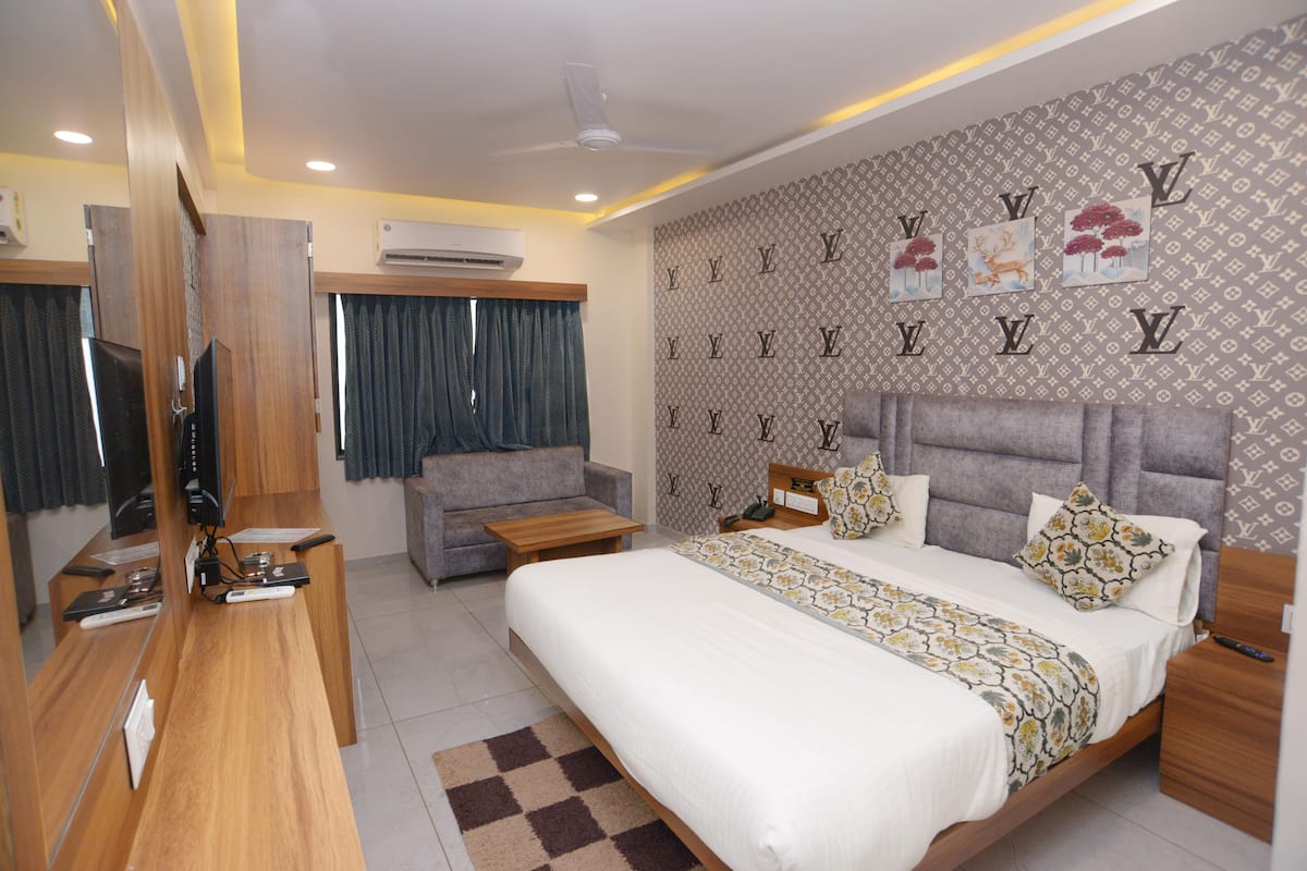 A hotel room with a bed, a desk, a chair, a TV, and a wall with a pattern.