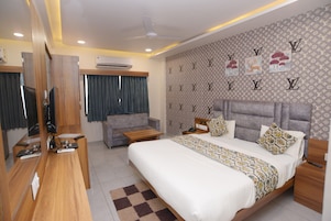 A hotel room with a bed, a desk, a chair, a TV, and a wall with a pattern.