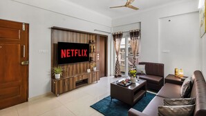 Ein modernes Wohnzimmer mit Flachbildfernseher, Deckenventilator und großem Fenster mit Vorhängen.