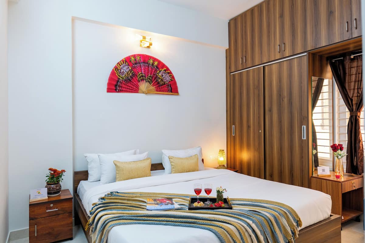 Una habitación de hotel con cama, armario de madera, mesita de noche y ventilador de pared.