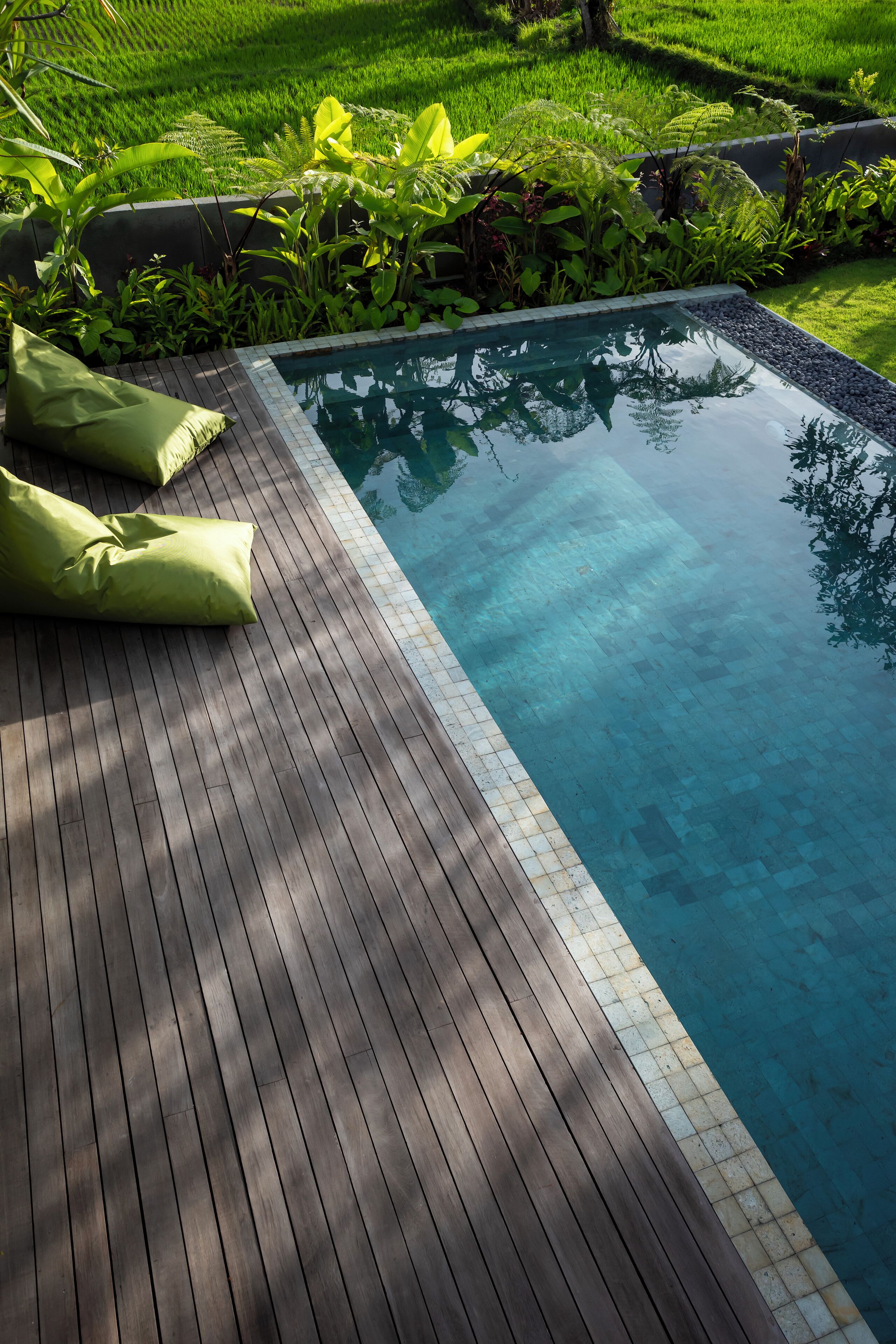 A wooden deck with a pool, surrounded by lush greenery.