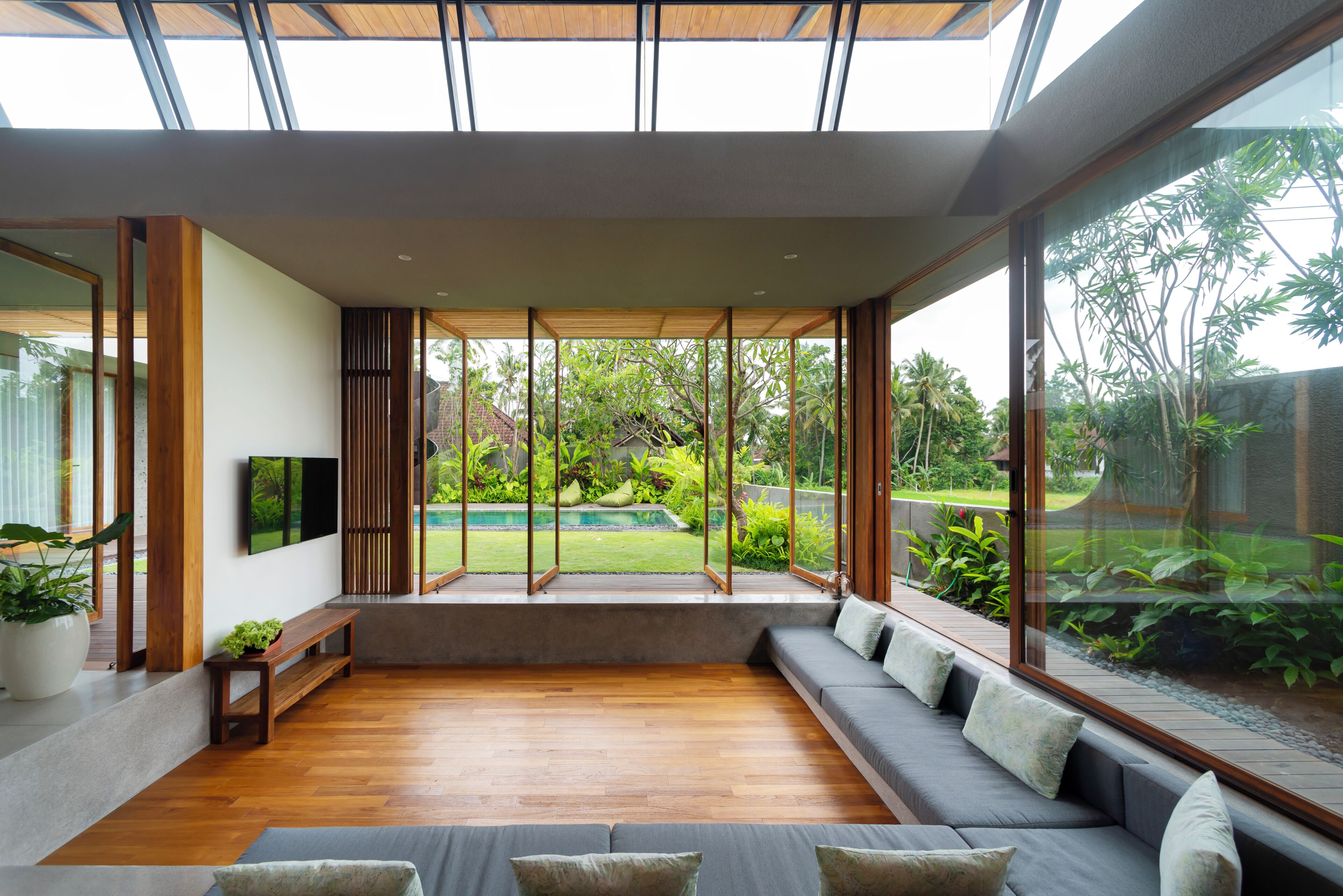 A modern living room with a large window, a sofa, a TV, and a wooden floor.
