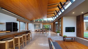 A modern kitchen with wooden bar stools, a dining area, and a large window providing natural light. - Indica Luxury Villa Ubud (Ubud)