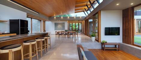 A modern kitchen with wooden bar stools, a dining area, and a large window providing natural light.
