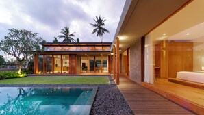 A modern house with a swimming pool, wooden deck, and a glass-enclosed porch. - Indica Luxury Villa Ubud (Ubud)