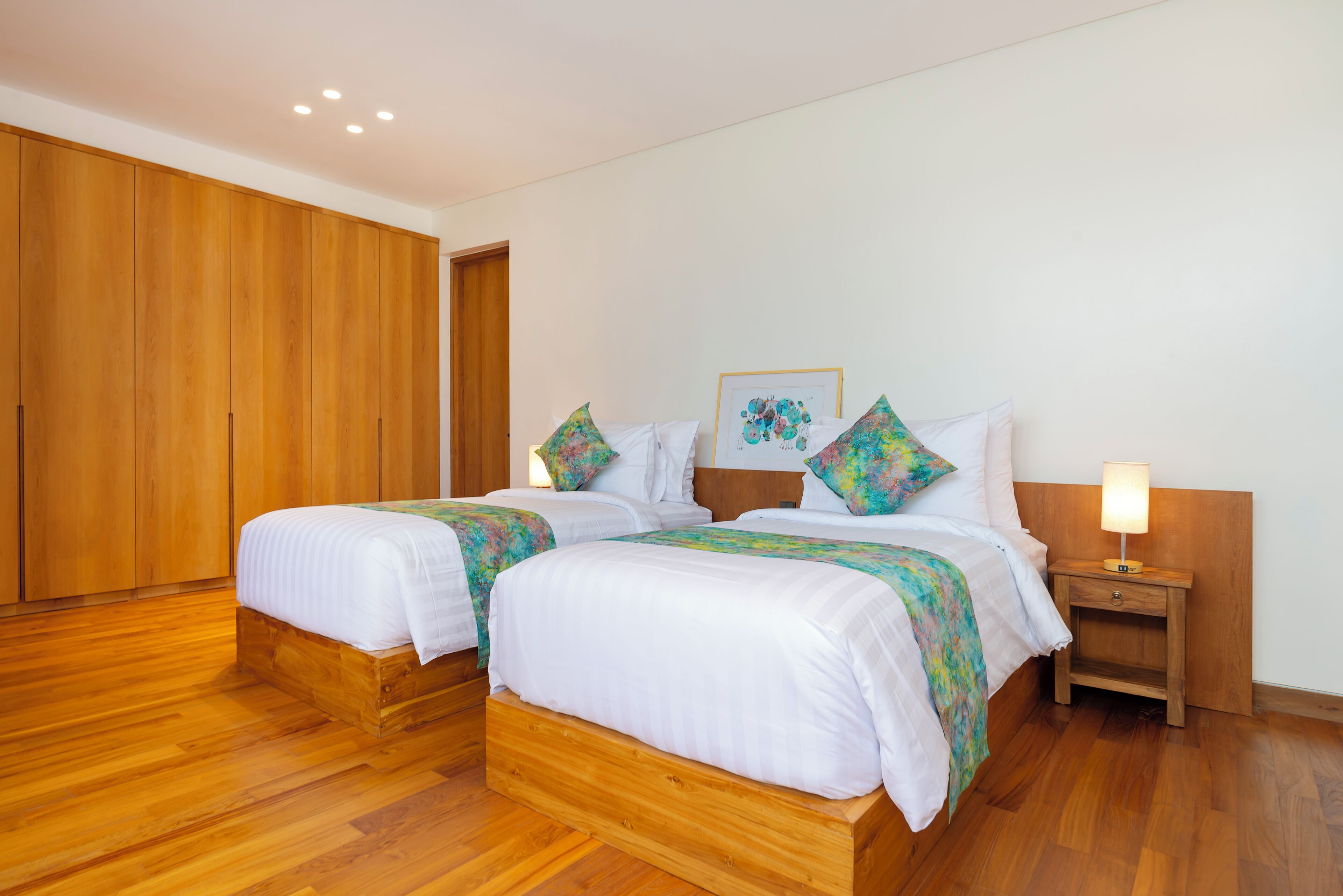 Une chambre double avec deux lits, un plancher en bois, une table de chevet avec une lampe et une armoire en bois.