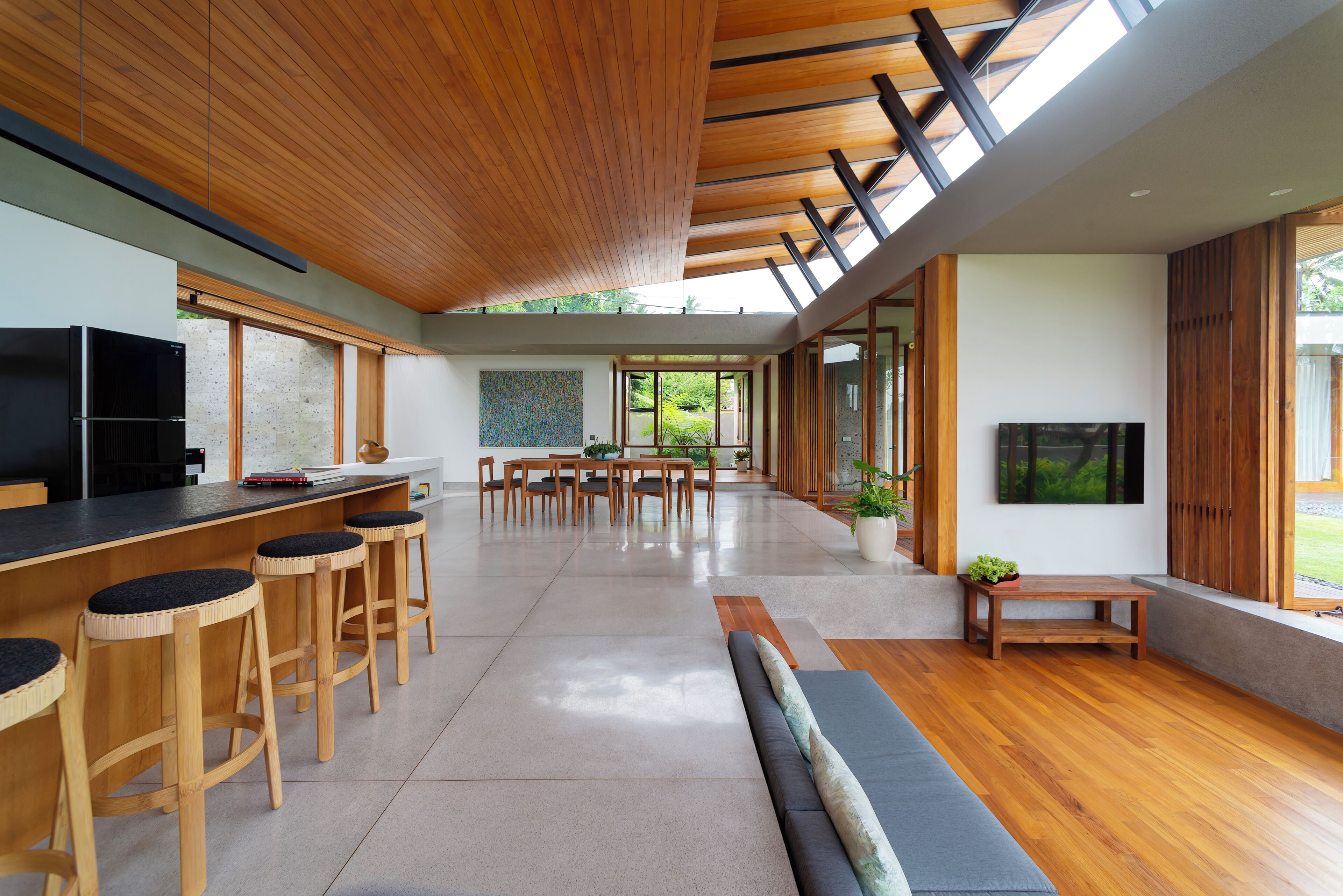 A modern kitchen with a black refrigerator, wooden stools, a dining table, and a TV.