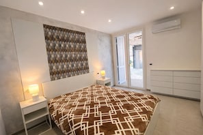 Ein Schlafzimmer mit Bett, Nachttischen, einem Wandbild, einer Schiebetür zum Außenbereich und einer fest installierten Klimaanlage.