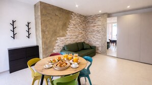 A modern living room with a stone accent wall, a green sofa, and a dining area with colorful chairs and breakfast items. - Cristallo Bilo 1 al Cavo (Rio Marina)
