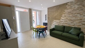 A modern living room with a green sofa, a dining table with colorful chairs, a flat-screen TV, and a stone-textured wall. - Cristallo Bilo 1 al Cavo (Rio Marina)