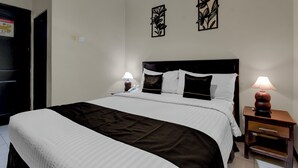 A neatly made bed with a white and brown bedspread, two wall-mounted black floral art pieces, a bedside lamp, and a small wooden nightstand with a lamp.