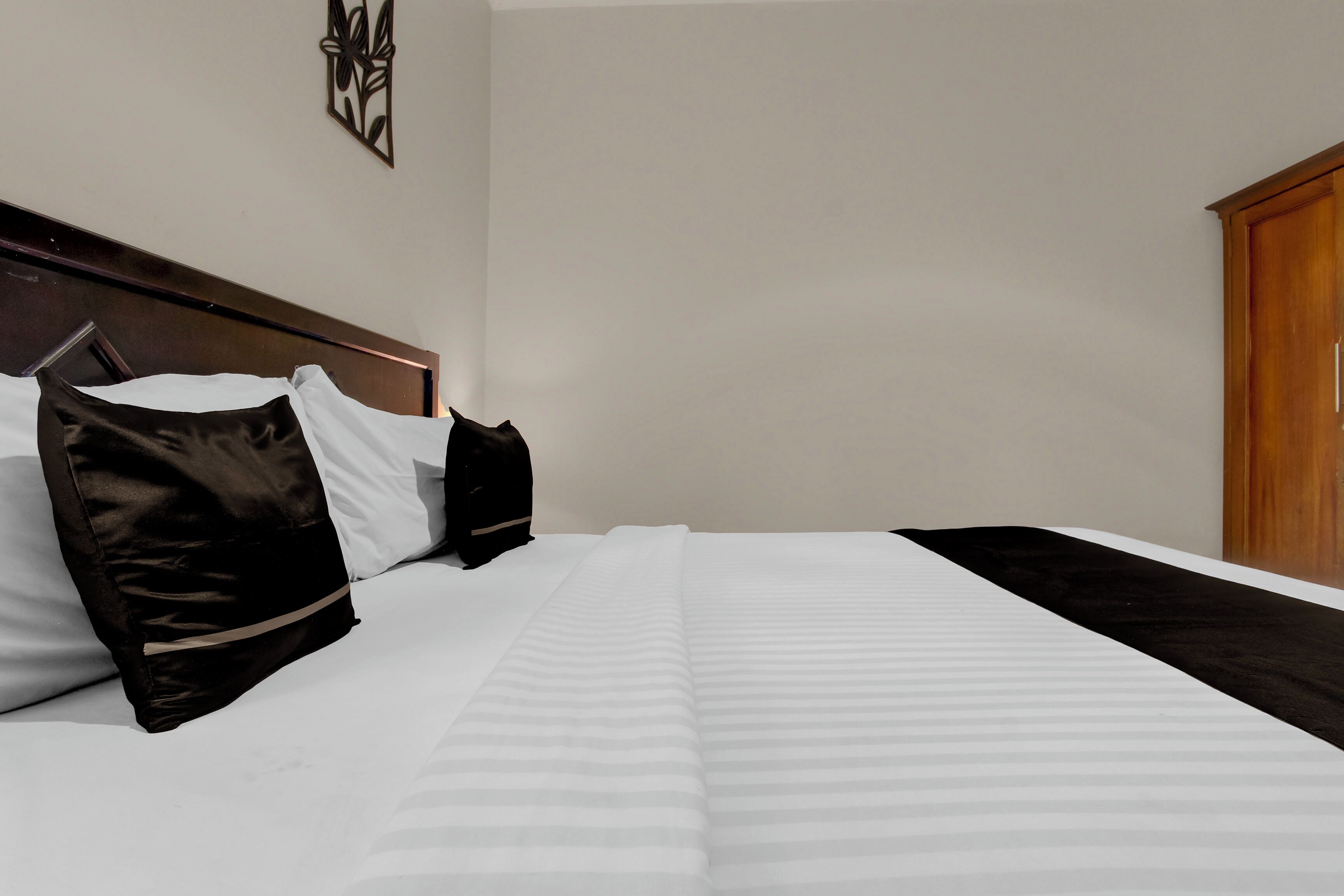 A neatly made bed with white and black bedding, a wooden headboard, and a wooden wardrobe.