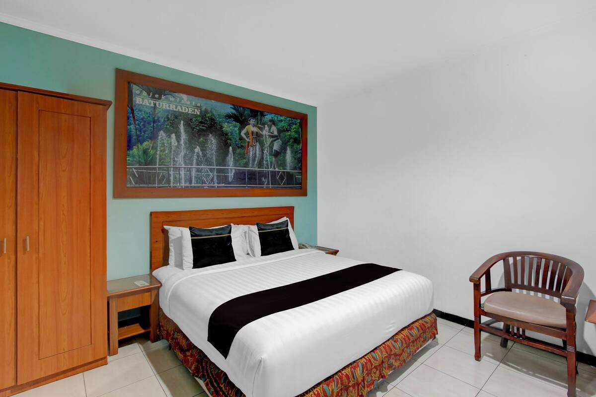 Ein Hotelzimmer mit Bett, Holzschrank, Stuhl und einem Bild an der Wand.