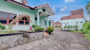 A residential street with a house featuring a tiled roof, a stone wall, and a paved walkway.