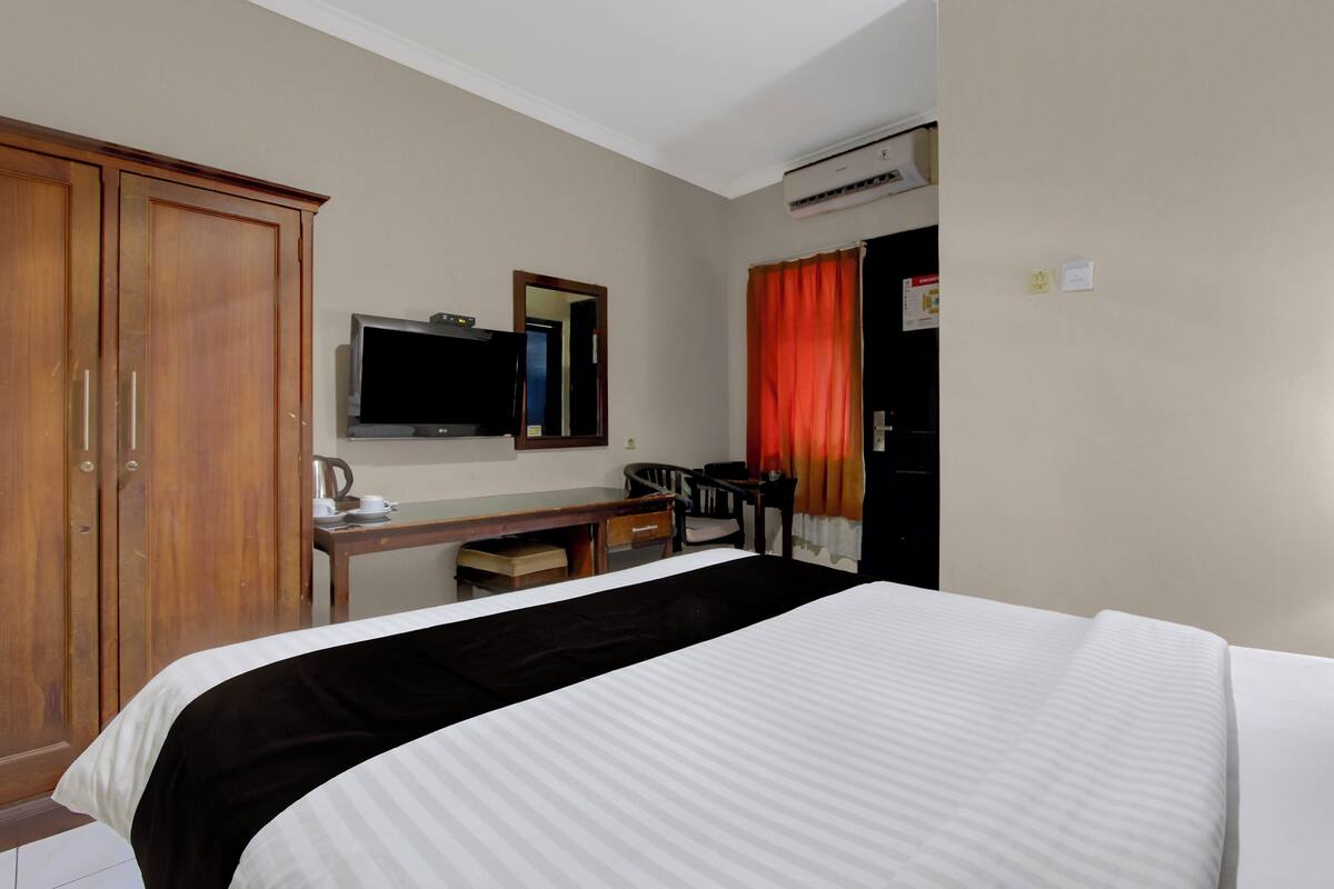 Ein Hotelzimmer mit Bett, Schreibtisch, Stuhl, Fernseher und Klimaanlage.