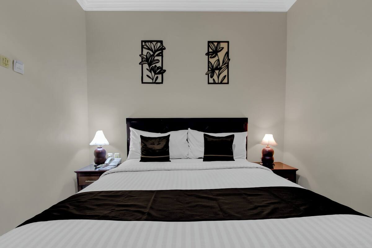 Ein ordentlich bezogenes Bett mit weißer und schwarzer Bettwäsche, zwei Nachttischlampen und zwei an der Wand befestigte Blumendekorationen.