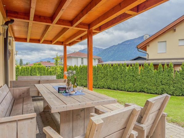 Un espace extérieur aménagé avec des meubles en bois, comprenant une table et des bancs, une bouteille de vin et un verre.
