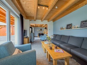 Un salon moderne avec un plafond en bois, un canapé gris, une table basse en bois et un téléviseur.