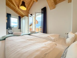 Une chambre avec deux lits, un plafond en bois, une fenêtre avec des rideaux et une vue sur l’extérieur.
